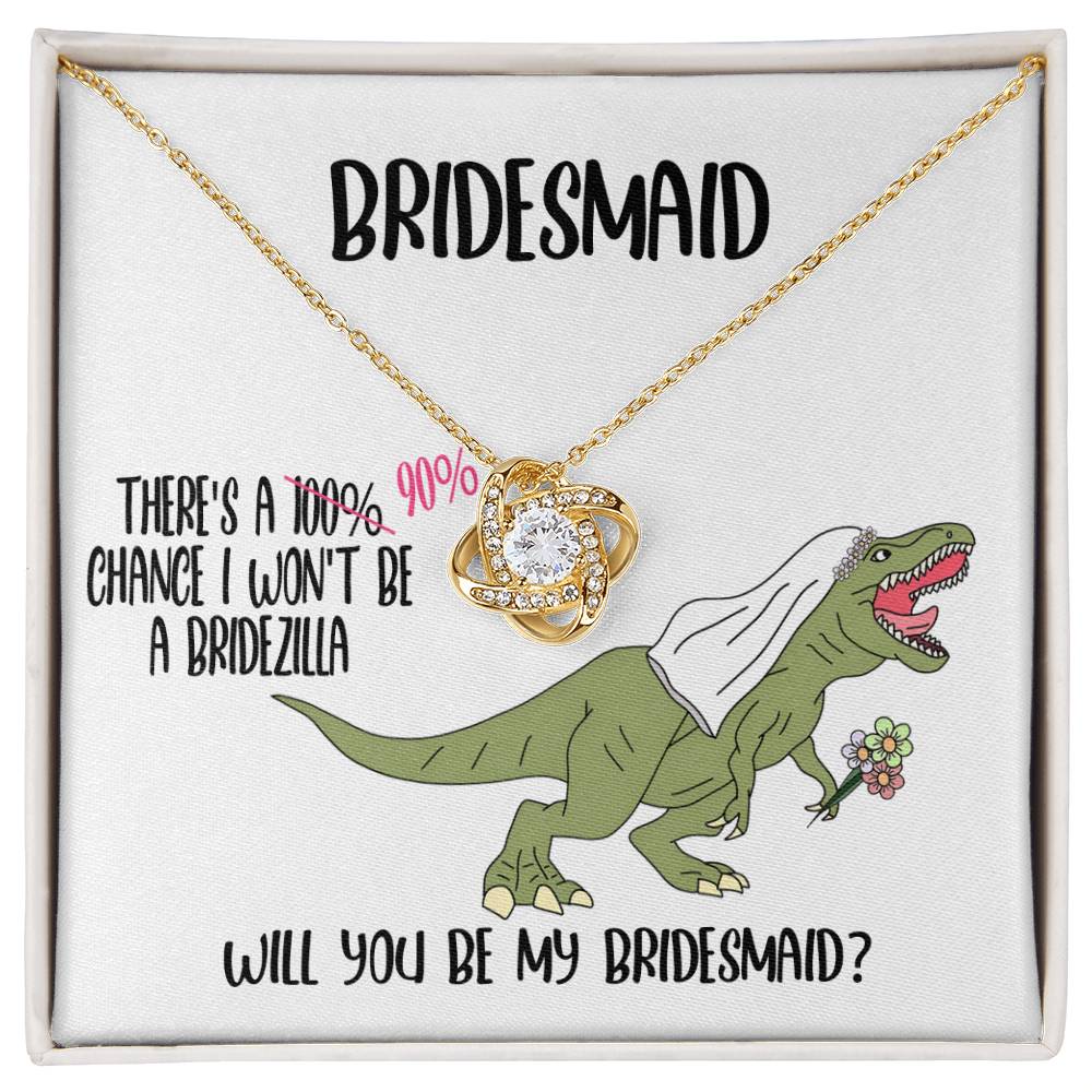 A bridesmaid proposal necklace box featuring a dinosaur with a veil and a stunning To Bridesmaid, Will You Be - Love Knot Necklace in white gold. The text reads, "There's a 90% chance I won't be a bridezilla. Will you be my bridesmaid?