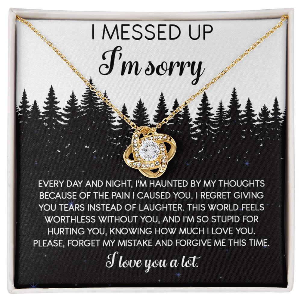 The Sorry-By My Thoughts - Love Knot Necklace, featuring a heart-shaped pendant adorned with cubic zirconia crystals, is displayed on a card with an apology message. The card reads: "I messed up. I'm sorry. Every day and night, I'm haunted...I love you a lot," set against a serene forest background.