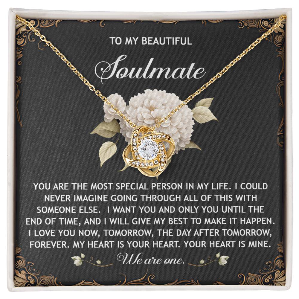 The Soulmate-We Are One Love Knot Necklace features a heart pendant on a black card with a white flower design and an affectionate soulmate message, elegantly crafted with cubic zirconia for a radiant gold finish.