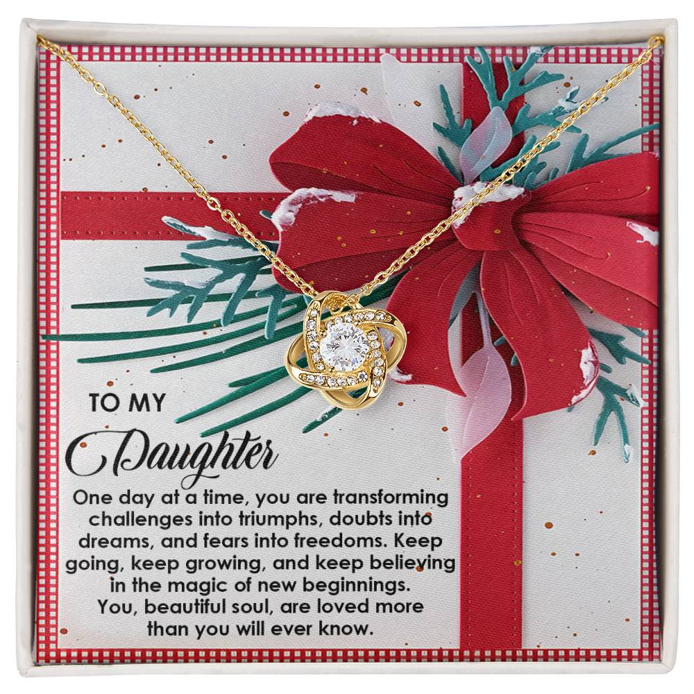 The Daughter-Beautiful Soul - Love Knot Necklace features a gold-finish pendant nestled inside a gift box with a red bow. Its sparkling cubic zirconia adds an elegant touch, while the heartfelt message inside encourages your daughter's growth and expresses profound love.