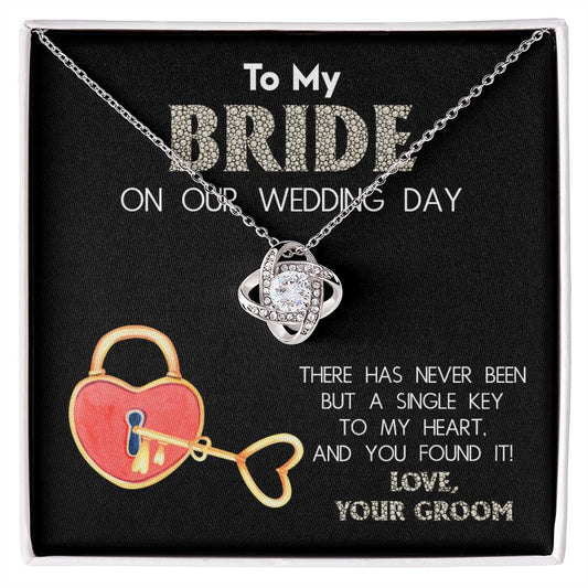 A "To My Bride, A Single Key - Love Knot Necklace" adorned with cubic zirconia crystals is displayed against a background with text that reads, "To My Bride On Our Wedding Day" and "There has never been but a single key to my heart, and you found it! Love, Your Groom.