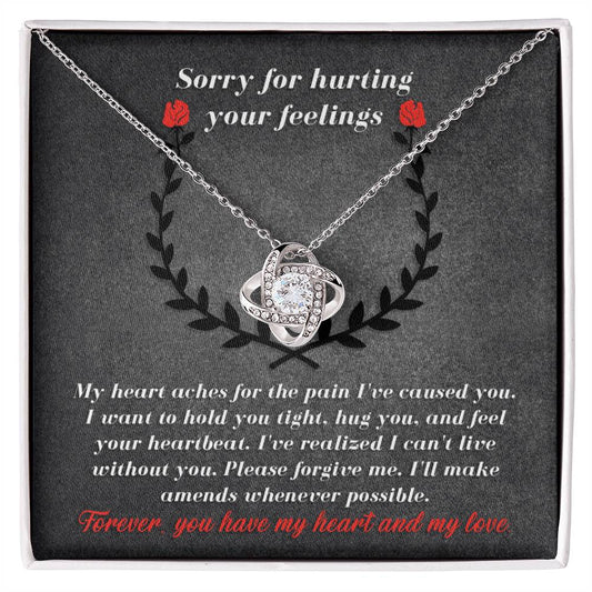 The "Sorry-Make Amends - Love Knot Necklace," featuring an intricate silver pendant adorned with cubic zirconia crystals, is displayed on a fabric background. At the top, "Sorry for hurting your feelings" is written, followed by an apology note in white text.