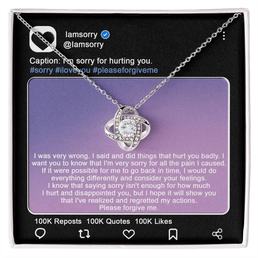 A stunning "Sorry-Hurt You Badly - Love Knot Necklace" in 14k white gold, adorned with cubic zirconia crystals, is displayed in front of a printed Instagram post that includes an apology message and hashtags like #sorry and #iloveyou.