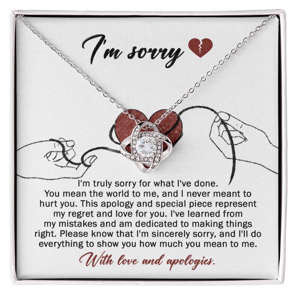 The Sorry-Mean The World - Love Knot Necklace, crafted from white gold and adorned with a heart-shaped pendant, is displayed on a card. This card conveys an apology message expressing regret and dedication to making things right, ending with "With love and apologies." The necklace is embellished with sparkling cubic zirconia crystals that add a touch of elegance.