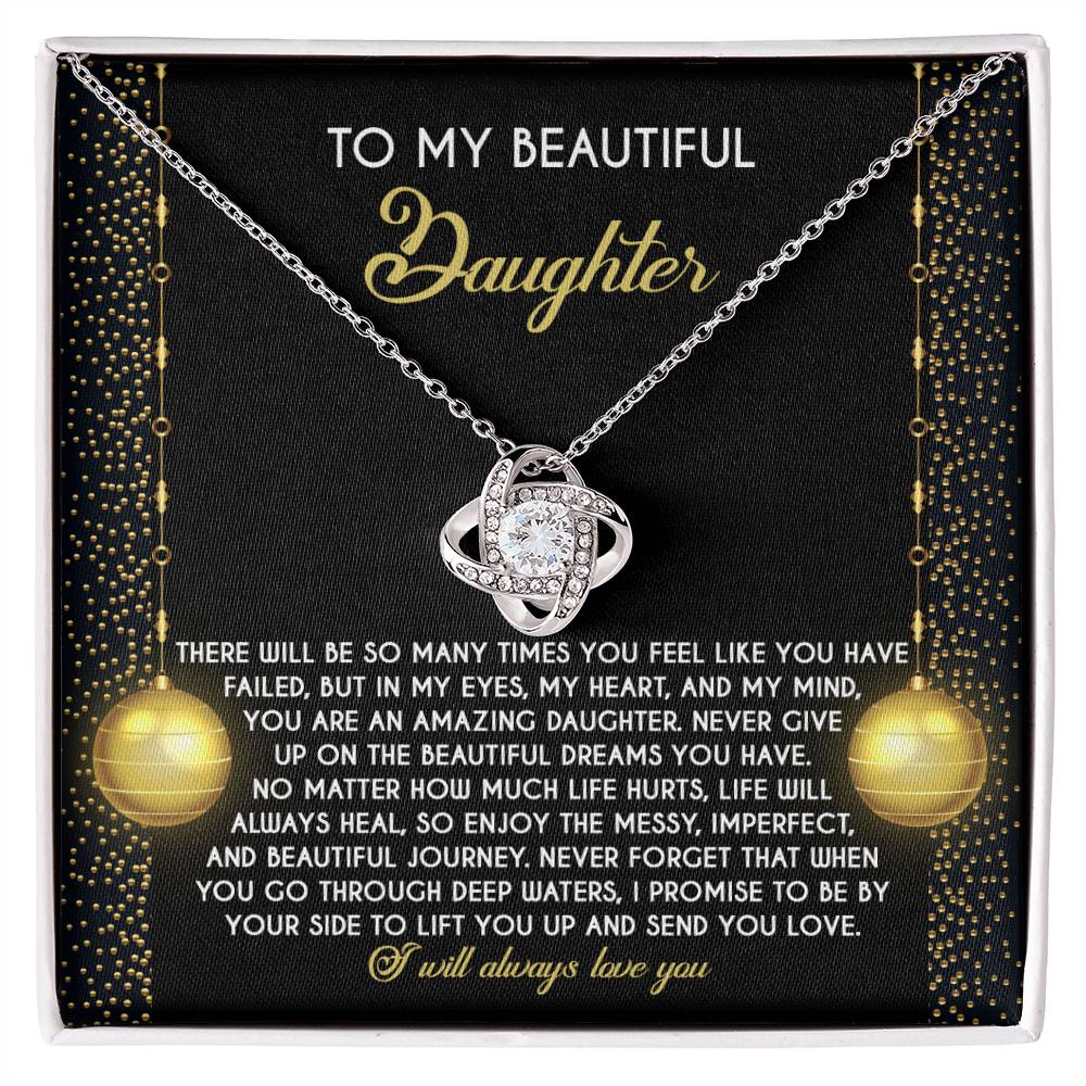 The Daughter-Deep Waters - Love Knot Necklace, accompanied by a heartfelt message for a daughter, is an elegantly personalized gift. It features a heart pendant displayed on a cushion and is beautifully adorned with sparkling cubic zirconia crystals, emphasizing love, perseverance, and support.