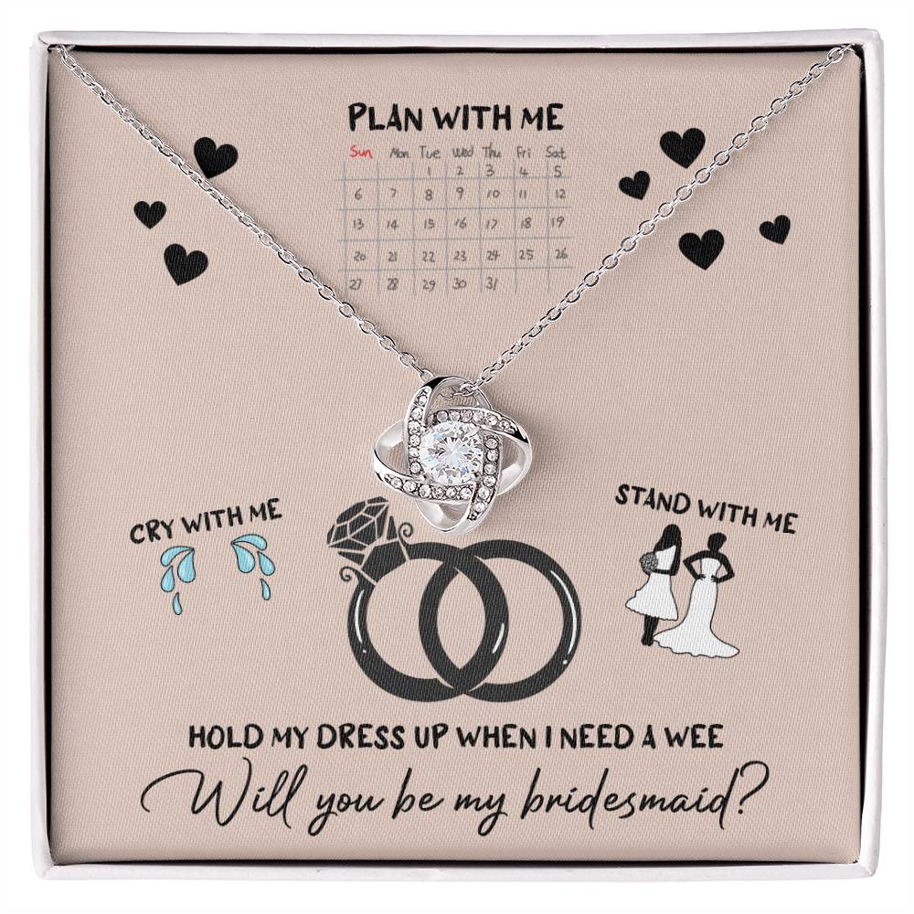 A To Bridesmaid, Will You Be 2 - Love Knot Necklace, adorned with cubic zirconia crystals, is displayed on a card featuring a calendar, wedding rings, and bridesmaid-related illustrations. The text reads, "Will you be my bridesmaid?" Choose from a white gold or yellow gold finish to make the moment even more special.