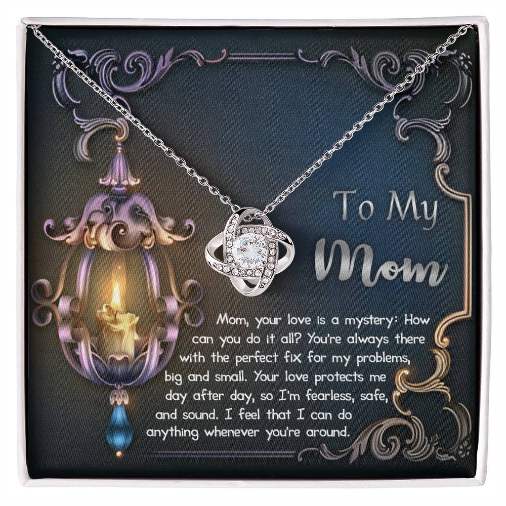 A To Mom, Love Is Mystery - Love Knot Necklace with a heart-shaped pendant inside a gift box featuring a printed poem dedicated to a mother, accompanied by an ornate candle and floral background.