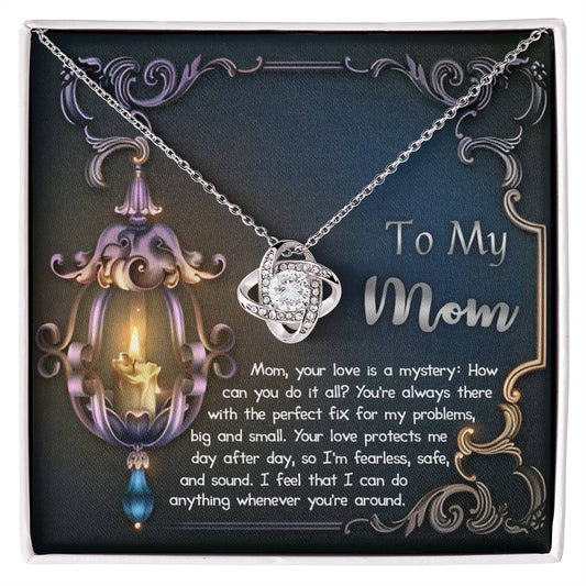 A To Mom, Love Is Mystery - Love Knot Necklace with a heart-shaped pendant inside a gift box featuring a printed poem dedicated to a mother, accompanied by an ornate candle and floral background.