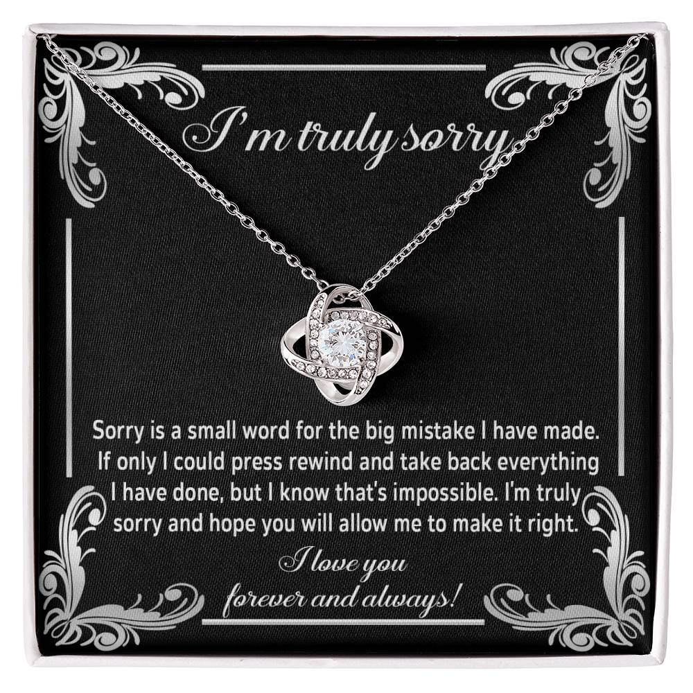 The "Sorry, Make It Right 2 - Love Knot Necklace" showcases a silver interlinked design on a black background. The backdrop features an apology message written in white text, complemented by the brilliance of cubic zirconia crystals.