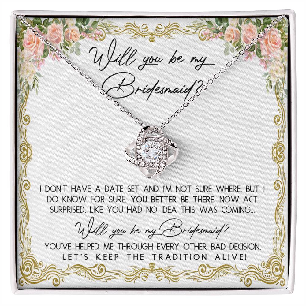 A To Bridesmaid, Keep The Tradition - Love Knot Necklace in a gift box with floral accents, featuring 14k white gold and cubic zirconia crystals. The message reads: "Will you be my Bridesmaid? I don't have a date set... act surprised. You've helped me through every other bad decision. Let's keep the tradition alive!