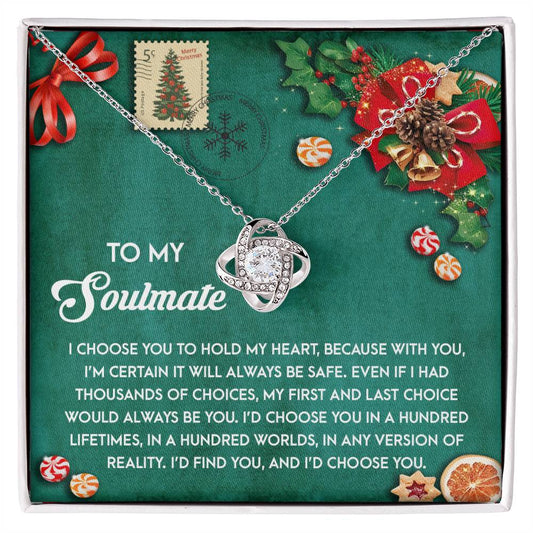 The Soulmate-Be Safe - Love Knot Necklace with a gold finish rests elegantly on a card featuring a heartfelt message, adorned with festive decorations and stamps.