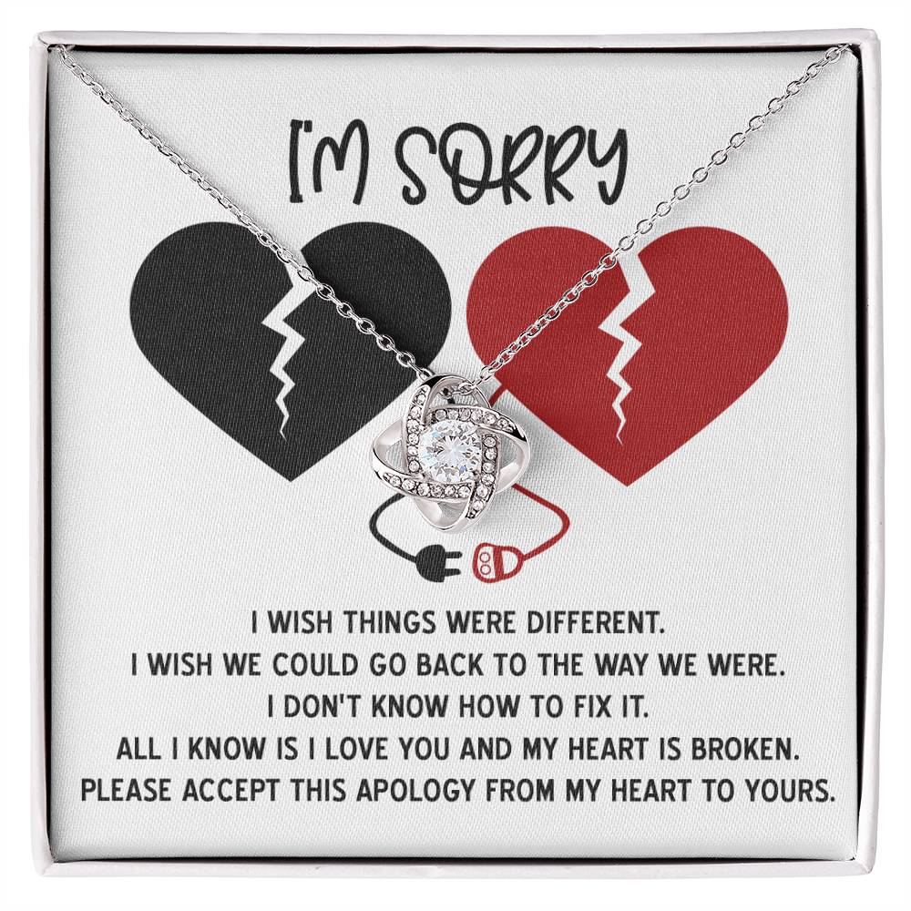 The "Sorry-Heart Is Broken - Love Knot Necklace" features an intertwined heart and infinity design, adorned with cubic zirconia crystals. It is displayed on a card with two broken hearts and a heartfelt message expressing sorrow and hope for reconciliation, all in a stunning white gold finish.