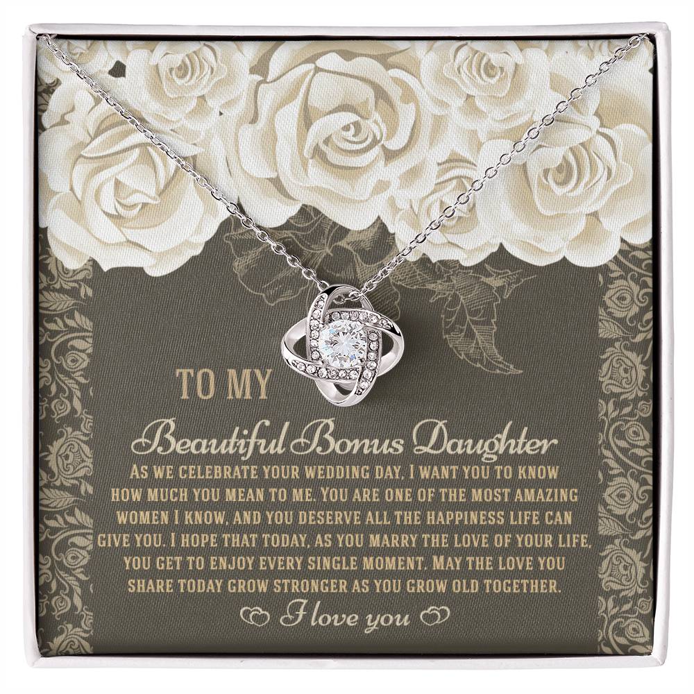 The "To Bonus Daughter, Grow Old Together - Love Knot Necklace" features a gold finish and sparkling cubic zirconia crystals. It comes packaged in a gift box decorated with an ornate floral design and includes a heartfelt message for your daughter on her wedding day.