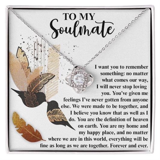 The Soulmate-Given Me Feelings - Love Knot Necklace features a heart-shaped pendant with a note that reads, "To My Soulmate," symbolizing eternal love and devotion. The design is adorned with feathers and bird illustrations, showcasing a stunning gold finish and sparkling cubic zirconia crystals for added elegance.