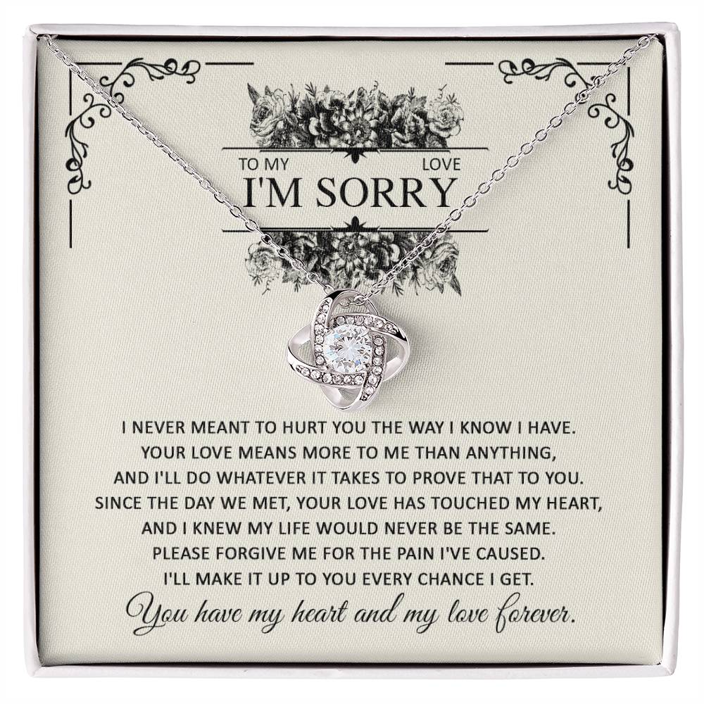 A gift box with the Sorry-Every Chance - Love Knot Necklace and an apology letter. The necklace, featuring a heart-shaped pendant with intertwined rings adorned with cubic zirconia crystals, comes in a dazzling white gold finish. The letter expresses regret and a promise of love.