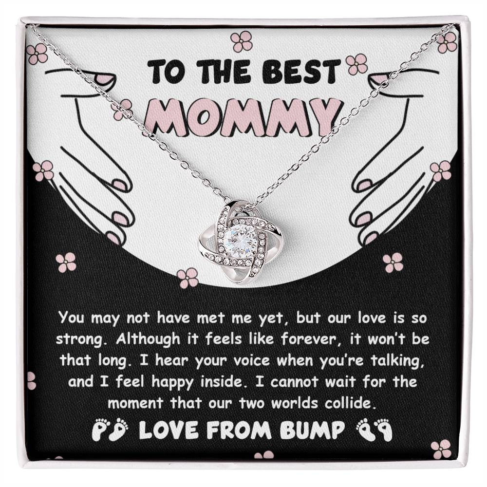 To Mom To Be, Two Worlds Collide - Love Knot Necklace: A silver necklace with a knot design adorned with cubic zirconia crystals in a gift box. It features a heartfelt message from an unborn child to their mother, expressing anticipation and love. The background showcases hands forming a heart, symbolizing their unbreakable bond.