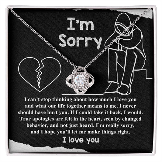 The "Sorry-Not Just Heard - Love Knot Necklace" features an apology message on a black background. The heartfelt text expresses regret and a promise to change, accompanied by illustrations of a heart and a person sitting with their head down. Cubic zirconia crystals add a touch of elegance, with "I love you" written at the bottom.