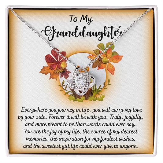 The Granddaughter-By Your Side - Love Knot Necklace, featuring a stunning gold finish and sparkling with cubic zirconia, is elegantly presented in a box adorned with an autumn leaf design. It's complemented by a heartfelt message for your granddaughter, capturing the essence of love and cherished memories.