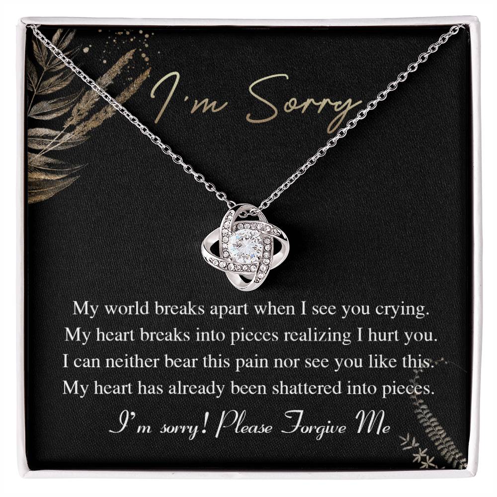 The Sorry-See You Crying - Love Knot Necklace, featuring an intertwined pendant adorned with cubic zirconia crystals, is elegantly displayed on a black card with the inscription "I'm Sorry" and an apology message in white text.