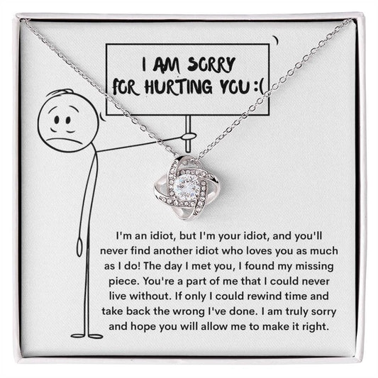 The Sorry-Missing Piece Love Knot Necklace is a silver necklace adorned with cubic zirconia crystals, featuring a heart-shaped pendant presented on a card with a stick figure holding a sign that reads "I am sorry for hurting you." Below the illustration, an apology message is included.