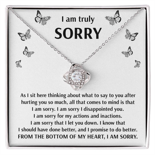 The Sorry-Done Better - Love Knot Necklace, featuring cubic zirconia crystals and a white gold finish, is elegantly presented in a box containing a heartfelt message. This message apologizes for causing hurt, expresses deep regret, and promises to improve, beginning with "I am truly sorry" and concluding with "I am sorry.