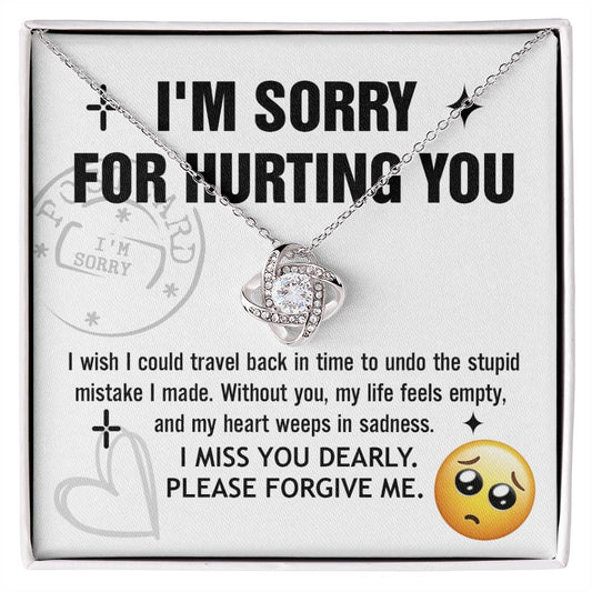 A Sorry-Travel Back - Love Knot Necklace with a white gold finish is displayed on a card featuring the text: "I'M SORRY FOR HURTING YOU," along with an apology note and a sad face emoji at the bottom right.