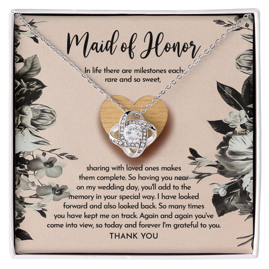 The "To Maid of Honor, My Wedding Day - Love Knot Necklace" features a heart-shaped pendant on a card titled "Maid of Honor," with a heartfelt message about milestones, love, and gratitude. The pendant is available in white gold or yellow gold finish and is adorned with sparkling cubic zirconia crystals.