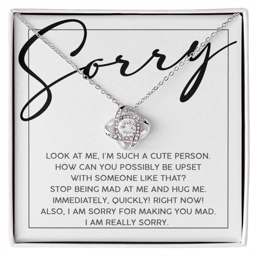 The Sorry-Someone Like That - Love Knot Necklace features a decorative pendant resting on a card inscribed with, "Sorry. Look at me, I'm such a cute person..." all elegantly presented in a jewelry box.