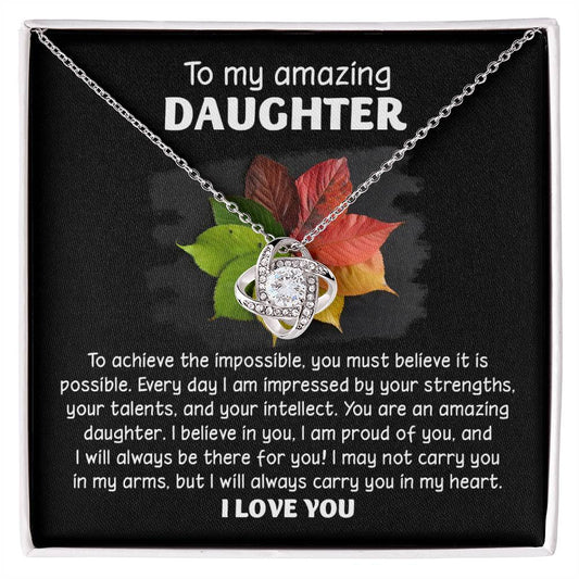 A box contains the "Daughter-It Is Possible - Love Knot Necklace" adorned with sparkling cubic zirconia crystals. The inside lid bears a heartfelt message to an amazing daughter, expressing love, admiration, and pride. The necklace is available in either a white gold or yellow gold finish, adding timeless elegance to this cherished gift.