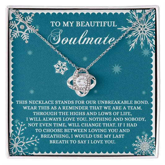 The Soulmate-A Team Love Knot Necklace, featuring a heart pendant embellished with shimmering Cubic Zirconia Crystals, is presented in a blue gift box titled "Soulmate," and includes a heartfelt message encircled by snowflakes.