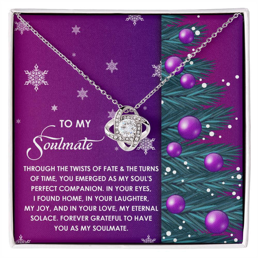 Introducing the Soulmate-Perfect Companion - Love Knot Necklace: This silver necklace, featuring a pendant, is elegantly displayed in a gift box that includes a heartfelt message for your soulmate. The backdrop, enhanced with decorative snowflakes and a pine tree branch design on a purple base, adds an enchanting touch. This piece shines with an exquisite gold finish and sparkling cubic zirconia accents.