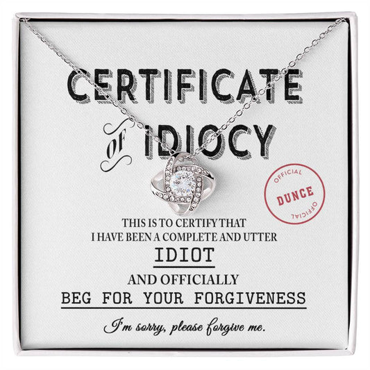 The Sorry-Certificate Of Idiocy - Love Knot Necklace rests on a card adorned with an apology message and an "Officially a Dunce" stamp.