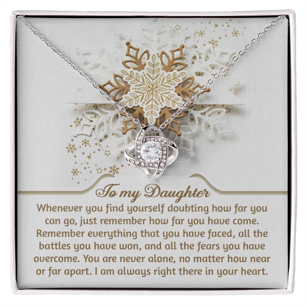 The Daughter-You Can Go - Love Knot Necklace features an elegant interlocking design and comes in a gift box with the message, "To my Daughter," alongside a heartfelt note about strength and support, symbolizing our unbreakable bond. It is embellished with cubic zirconia crystals and has a snowflake decoration in the background.