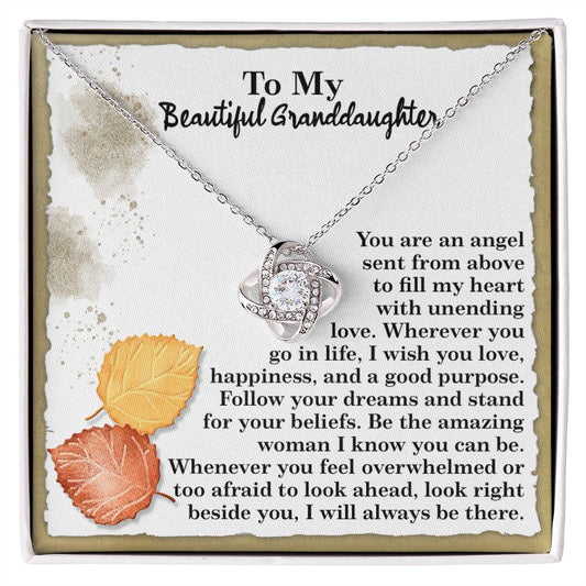 The Granddaughter-An Angel - Love Knot Necklace features a heart-shaped pendant embellished with cubic zirconia crystals, beautifully presented on a card with a heartfelt message to a granddaughter, and accented by two autumn leaves.