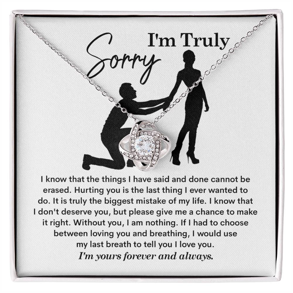 The Sorry-My Last Breath - Love Knot Necklace, a silver piece featuring an intertwined heart pendant decorated with cubic zirconia crystals, is presented on a card. The card includes an apology note with the phrase "I'm Truly Sorry" and the silhouette of one person kneeling before another.