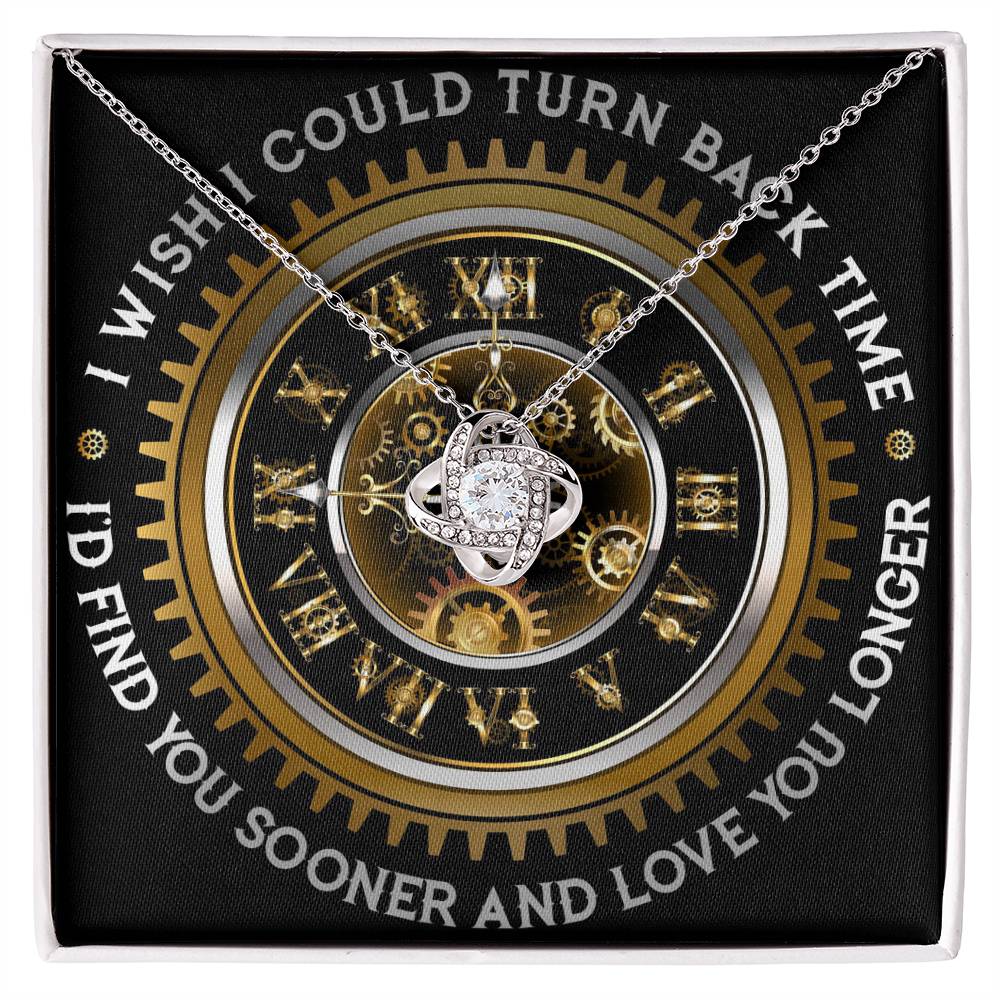 The "To Wife, Turn Back Time - Love Knot Necklace," adorned with cubic zirconia crystals, is elegantly displayed against a clock design backdrop. The text around the clock reads, "I WISH I COULD TURN BACK TIME, I'D FIND YOU SOONER AND LOVE YOU LONGER.