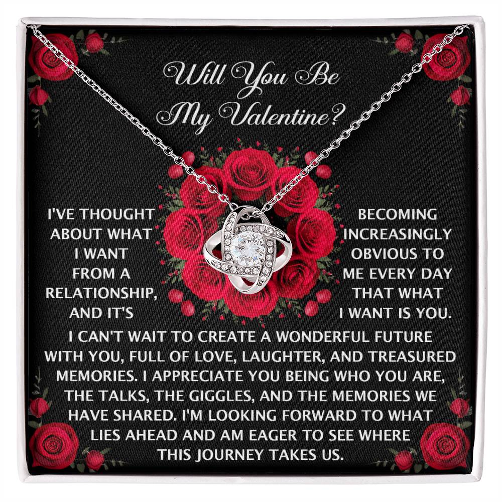 The "Soulmate-What I Want - Love Knot Necklace" elegantly rests on a box with a romantic message, adorned with cubic zirconia crystals and surrounded by red roses, asking, "Will You Be My Valentine?.