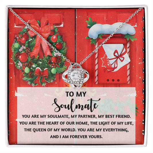 The Soulmate-Our Home - Love Knot Necklace, adorned with a heart pendant and cubic zirconia crystals, is elegantly showcased in a gift box. The box is decorated with a festive design featuring wreaths and a heartfelt message about a soulmate, making it the ideal personalized gift.
