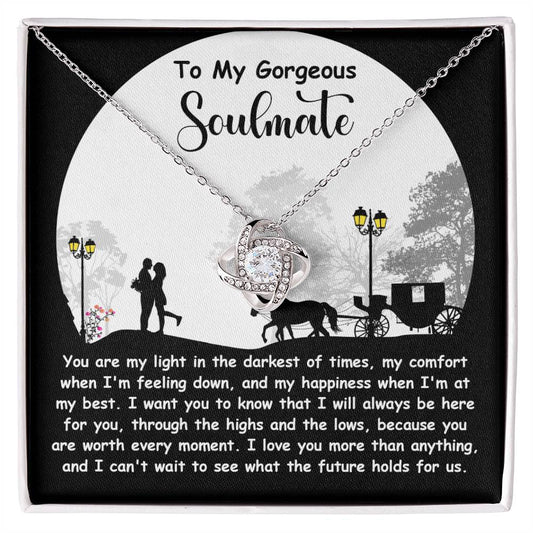 The Soulmate-Holds For Us - Love Knot Necklace boasts a twisted pendant adorned with sparkling cubic zirconia crystals, elegantly displayed on a card with a romantic message about soulmates, featuring an illustrated silhouette of a couple, trees, and a carriage.