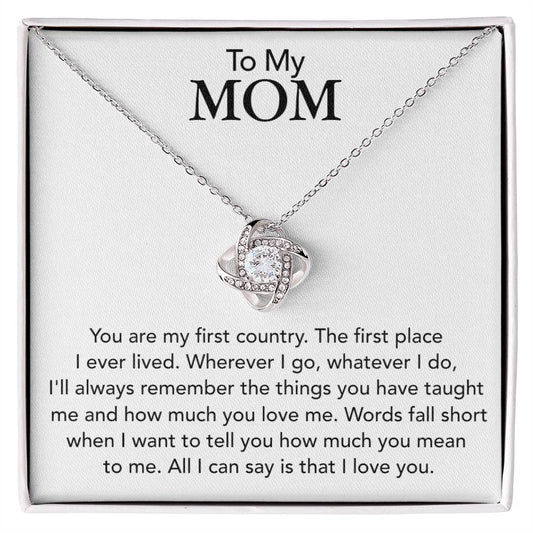 A To My Mom, You Are My First Country - Love Knot Necklace with cubic zirconia crystals presented in a gift box with a sentimental message addressed to 'my mom'.