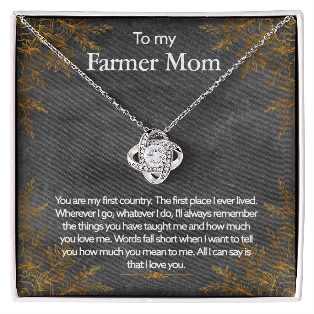 A silver "To My Farmer Mom, You Are My First Country" Love Knot Necklace with cubic zirconia crystals, accompanied by a personalized affectionate message to a mother with a farming background, displayed on a dark floral background from ShineOn Fulfillment.