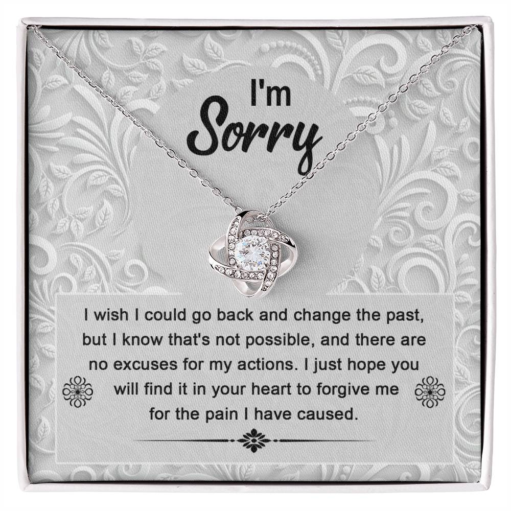 The Sorry-Change The Past - Love Knot Necklace with a white gold finish sits in a box with an apology message that reads, "I'm Sorry. I wish I could go back and change the past... I just hope you will find it in your heart to forgive me." The pendant sparkles with cubic zirconia crystals, symbolizing the unbreakable bond of love.