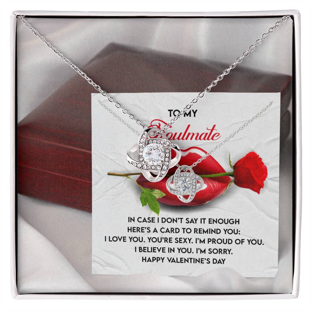 The Soulmate-Don't Say It Love Knot Necklace showcases interlocking rings with cubic zirconia crystals, set against a romantic card. It symbolizes an unbreakable bond, enhanced by a red rose and elegant red gift box background.