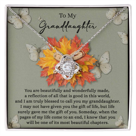 The Granddaughter-Gift Of You - Love Knot Necklace showcases a heart-shaped pendant embellished with sparkling Cubic Zirconia Crystals. It's presented on a card featuring a heartfelt message for your granddaughter, tastefully complemented by autumn leaves and butterflies in the background.