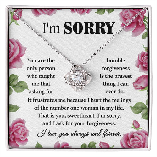 The Sorry-Your Forgiveness - Love Knot Necklace, adorned with cubic zirconia crystals and crafted in 14k white gold, is elegantly displayed against a floral background. The accompanying apology message reads, "I'm SORRY. I hurt the feelings of the number one woman in my life. I love you always and forever.