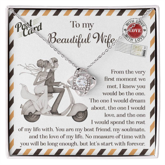 A 14k white gold To Wife, Be The One - Love Knot Necklace with cubic zirconia crystals is placed on a card depicting a couple on a scooter. The card features a heartfelt message to a wife, expressing love and commitment.