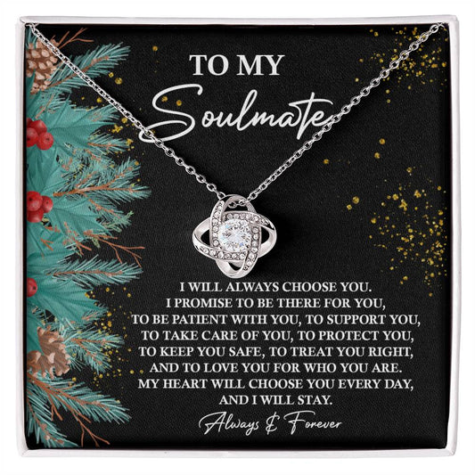 The Soulmate-Treat You Right - Love Knot Necklace, featuring an entwined heart pendant and sparkling cubic zirconia crystals, is elegantly displayed against a card titled "To My Soulmate." The backdrop, decorated with pine branches and gold accents, enhances the charm and elegance of this personalized gift.