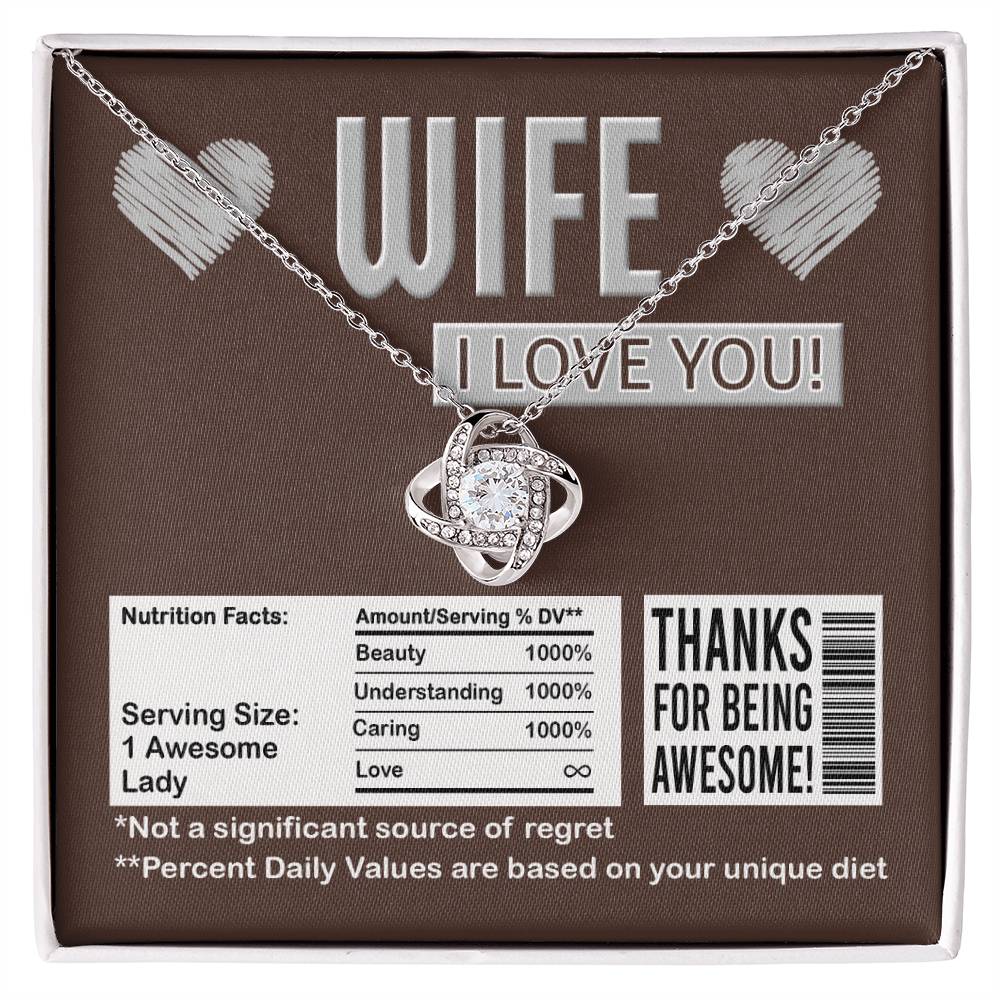 A To Wife, Nutrition Facts - Love Knot Necklace in a gift box that reads, "WIFE I LOVE YOU!" and "Thanks for being awesome!" It humorously lists nutritional facts like "Beauty 1000%" and "Not a significant source of regret," featuring sparkling cubic zirconia crystals with a stunning gold finish.