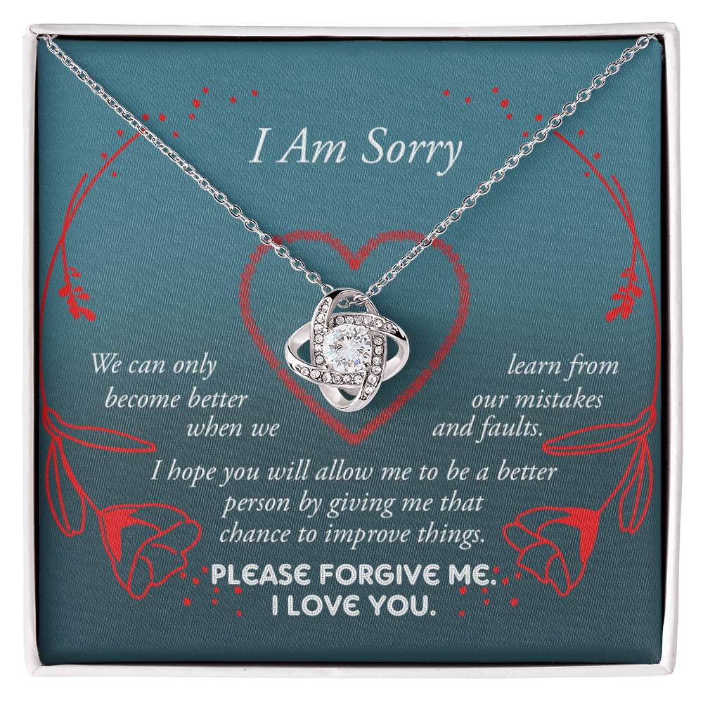 The Sorry-Mistakes And Faults - Love Knot Necklace, featuring a heart-shaped pendant with sparkling cubic zirconia set in white gold, is elegantly presented in a box adorned with the words "I Am Sorry" and a heartfelt apology message.