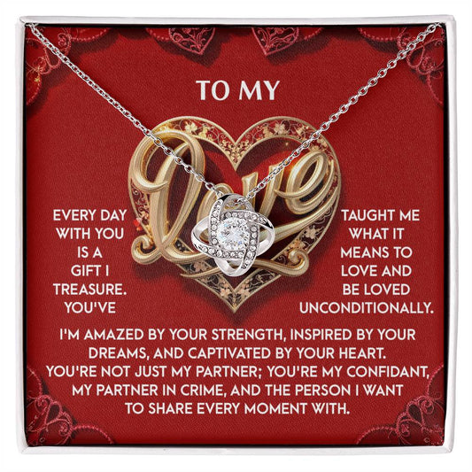 The "My Love-Every Moment - Love Knot Necklace" features a silver design with an intricate pendant adorned with cubic zirconia, set against a red background. The display includes a heartfelt message emphasizing "LOVE," making it an ideal personalized gift.